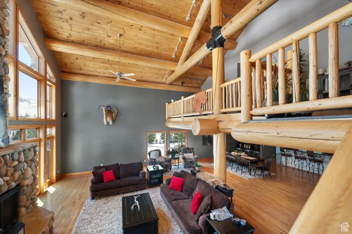 Living area with a wooden ceiling with exposed beams, a ceiling fan, wood finished floors, a stone fireplace, and high vaulted ceiling