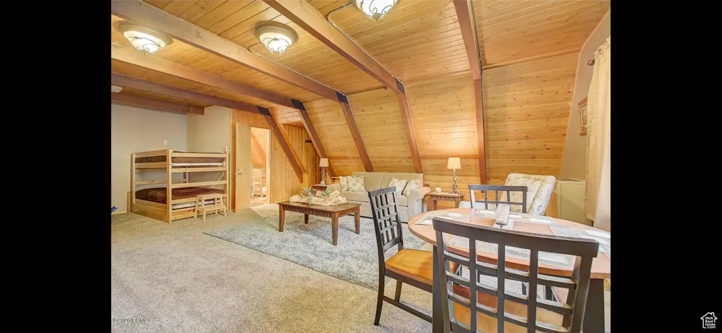 Living area featuring a wood ceiling with exposed beams, carpet floors, and wood walls