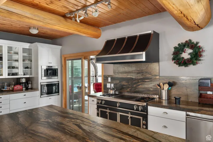Kitchen featuring dark countertops, range hood, stove, a wooden ceiling with exposed beams, and tasteful backsplash