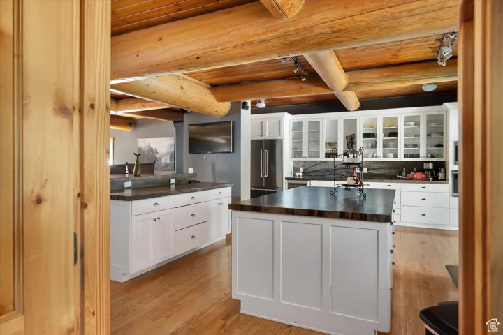 Kitchen with dark countertops, a wooden ceiling with exposed beams, light wood-style floors, high end fridge, and a center island with sink