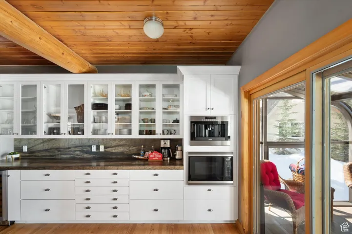 Bar area with a wood ceiling with exposed beams, black microwave, decorative backsplash, beverage cooler, and wood finished floors
