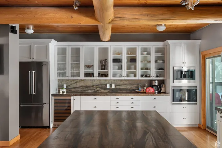 Kitchen featuring dark countertops, high quality fridge, beverage cooler, light wood-style flooring, and glass insert cabinets