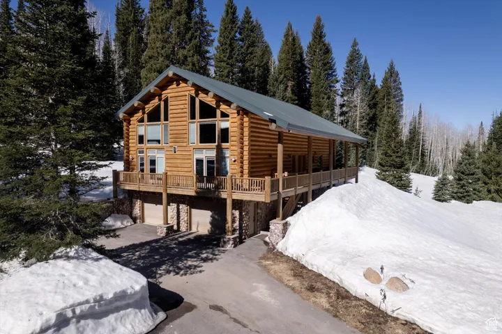 View of front of property featuring log exterior, stone siding, asphalt driveway, and a forest view