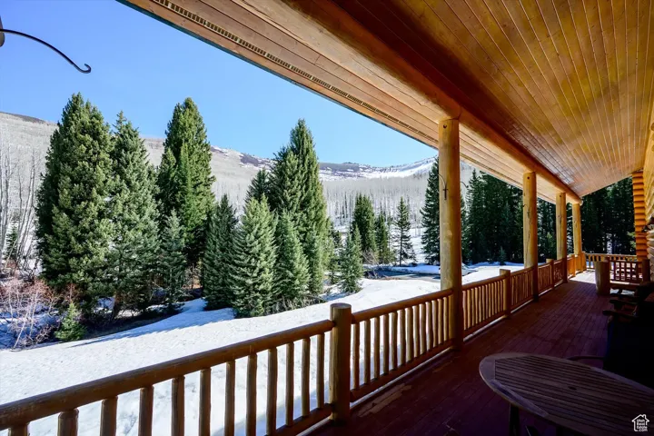 Snow covered deck featuring a mountain view, a porch, and a forest view