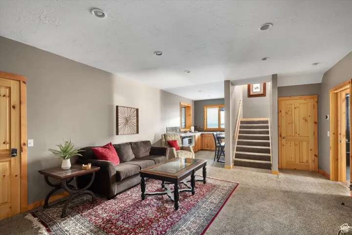Living area featuring stairs, light colored carpet, and a textured ceiling