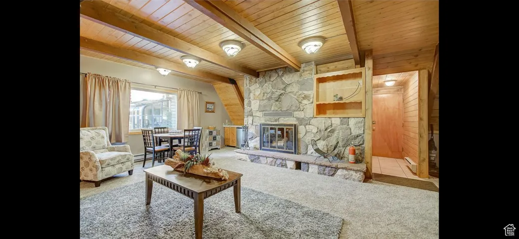 Carpeted living area featuring a wood ceiling with exposed beams, a stone fireplace, and baseboard heating