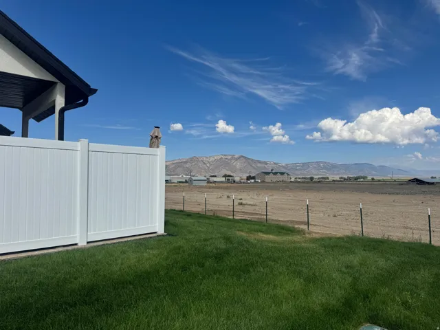 Manicured lawn, white privacy fencing, dark roofline, distant mountain landscape, and open fields