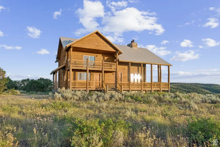 Back of property with a metal roof, a chimney, a deck, and a balcony