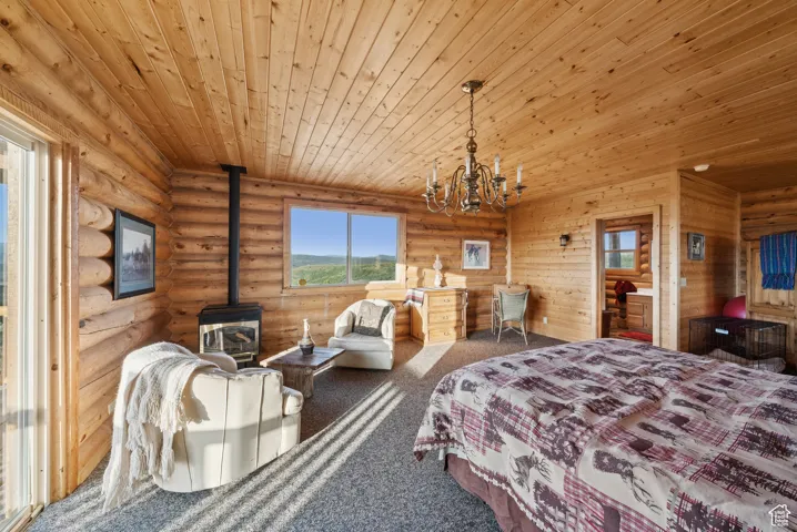 Bedroom with a wood stove, wooden ceiling, multiple windows, carpet, and a chandelier