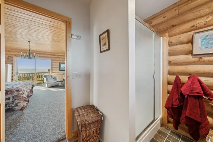 Bathroom with rustic walls, a stall shower, and a chandelier