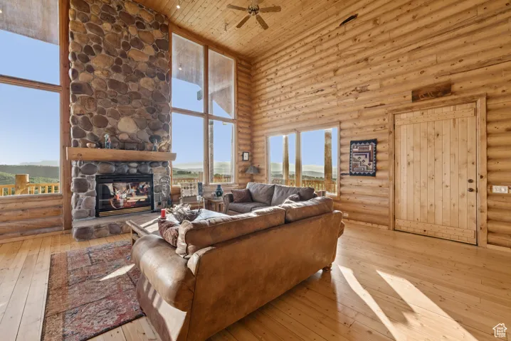 Living room with a towering ceiling, log walls, ceiling fan, hardwood / wood-style floors, and plenty of natural light
