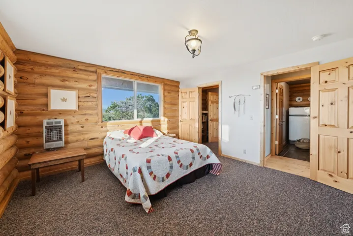Carpeted bedroom with rustic walls, heating unit, and freestanding refrigerator
