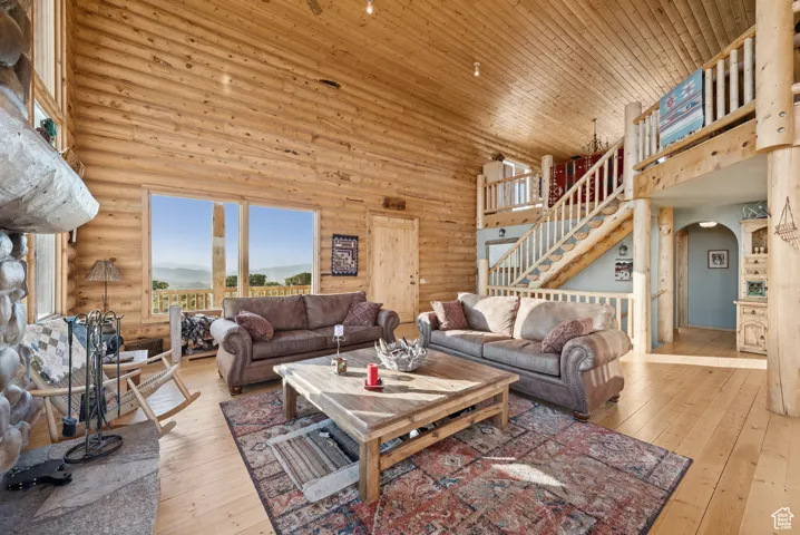 Living area featuring high vaulted ceiling, arched walkways, log walls, wood-type flooring, and stairway