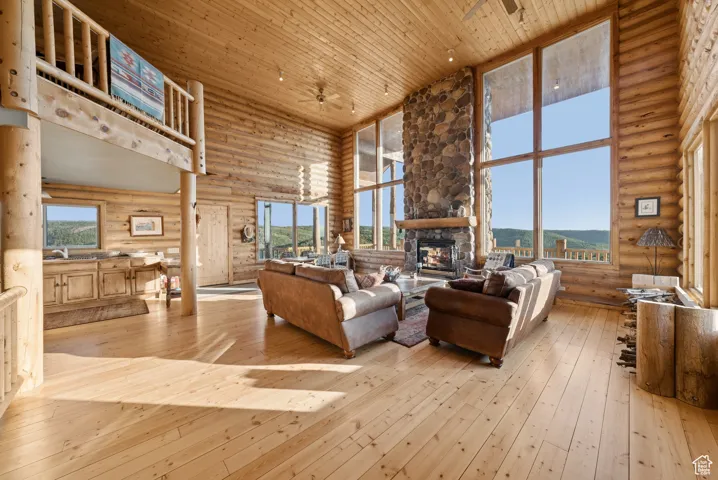 Living area featuring a towering ceiling, log walls, wooden ceiling, a fireplace, and ceiling fan
