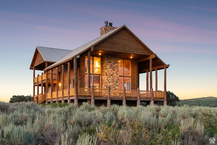 Back of property at dusk featuring a chimney, a metal roof, faux log siding, and stone siding