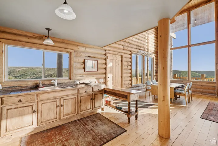 Kitchen with rustic walls, light wood-style floors, hanging light fixtures, and light brown cabinets
