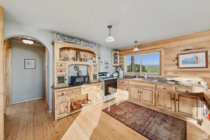 Kitchen with arched walkways, white gas stove, light wood-style floors, open shelves, and hanging light fixtures
