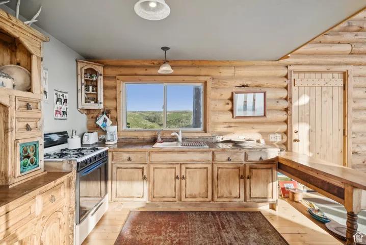 Kitchen featuring gas range, light wood-style floors, log walls, and decorative light fixtures