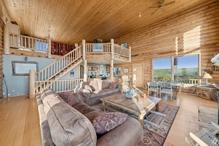 Living room featuring log walls, a high ceiling, hardwood / wood-style floors, wooden ceiling, and a ceiling fan