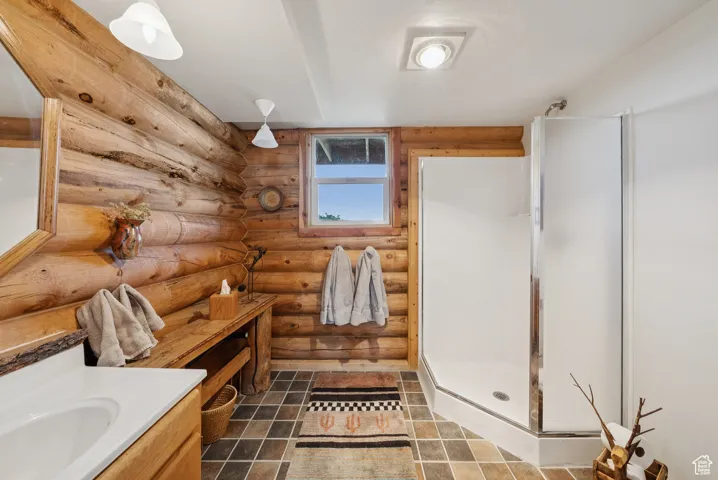 Full bath with log walls, a stall shower, and vanity