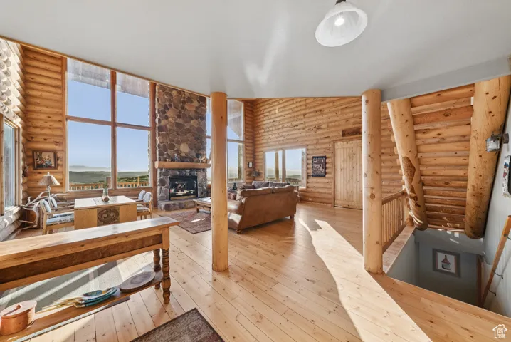 Living area with log walls, a fireplace, hardwood / wood-style floors, healthy amount of natural light, and a high ceiling
