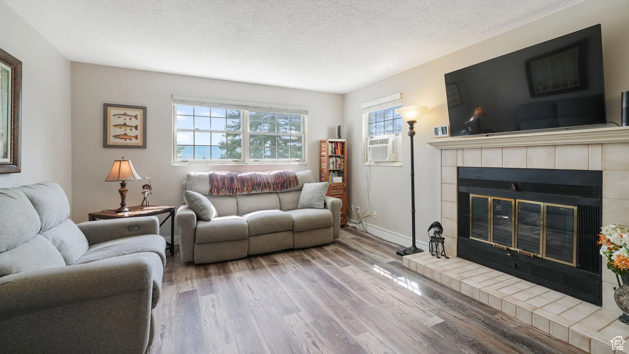 Living area featuring wood finished floors, a tile fireplace, a textured ceiling, and cooling unit