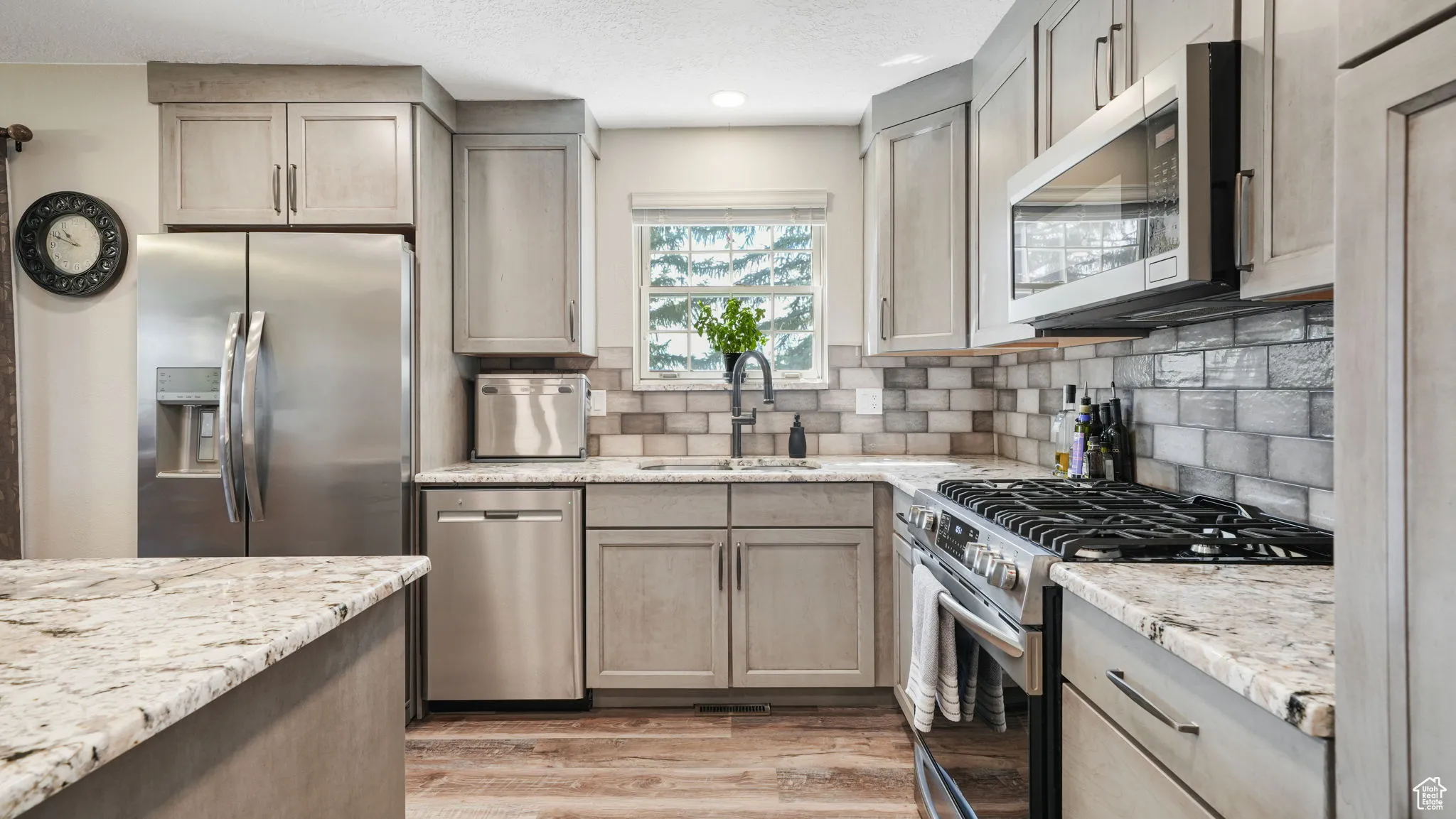 Kitchen featuring appliances with stainless steel finishes, light wood-style floors, tasteful backsplash, light stone counters, and gray cabinets