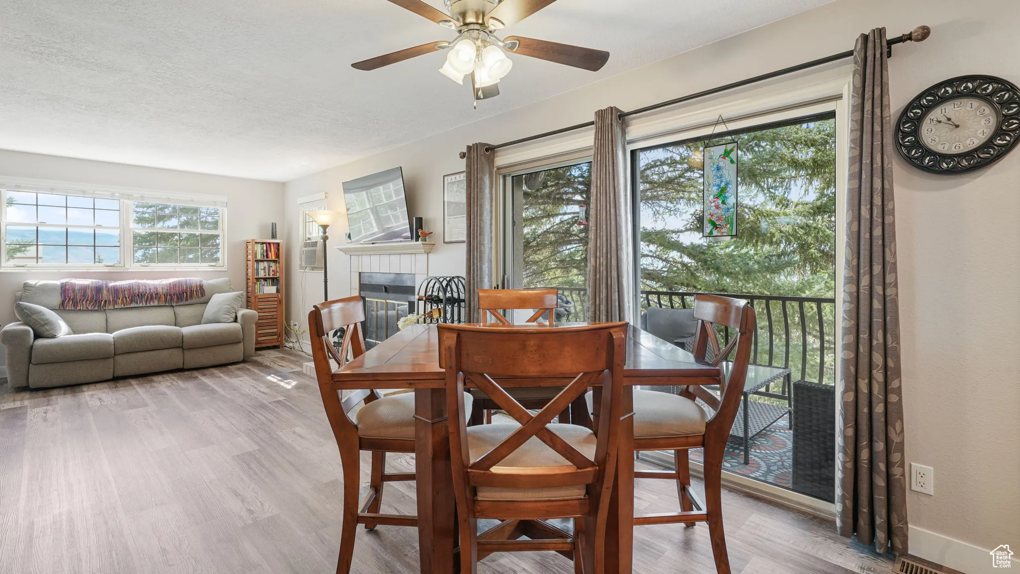 Dining room featuring ceiling fan, wood finished floors, a tiled fireplace, and a textured ceiling