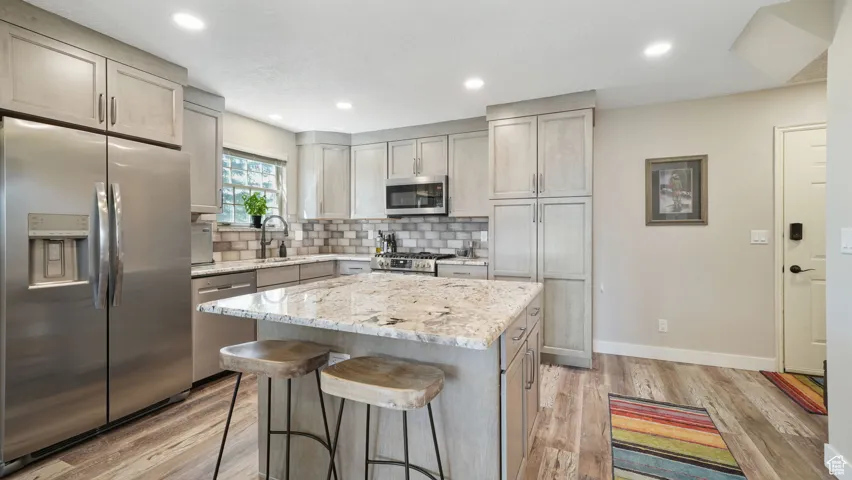 Kitchen with appliances with stainless steel finishes, light wood-style flooring, a breakfast bar area, backsplash, and recessed lighting