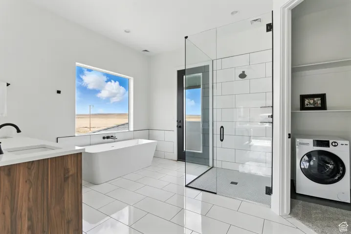 Bathroom featuring washer / dryer, a shower stall, a soaking tub, tile walls, and vanity