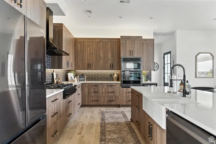 Kitchen with light countertops, wall chimney exhaust hood, light wood-type flooring, and backsplash