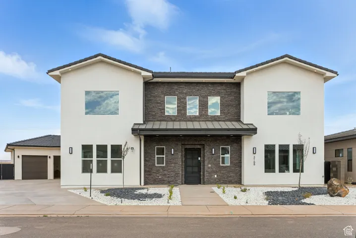 View of front facade featuring stone siding, stucco siding, driveway, a garage, and a standing seam roof
