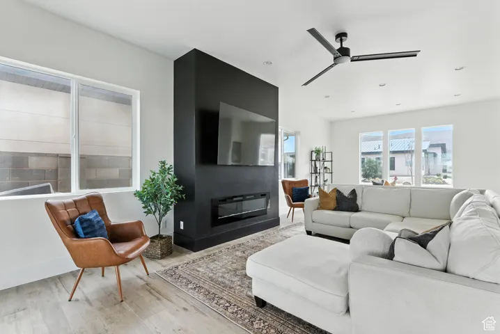 Living area featuring wood finished floors, a glass covered fireplace, and a ceiling fan