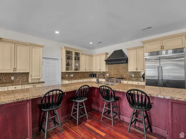 Kitchen with cream cabinets, stainless steel built in fridge, hardwood floors,  decorative backsplash, and recessed lighting