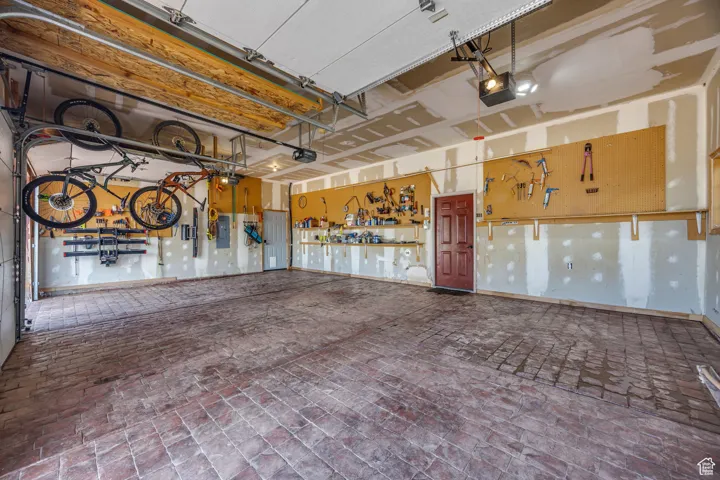 Garage featuring stamped concrete, a garage door opener, electric panel, and a workshop area