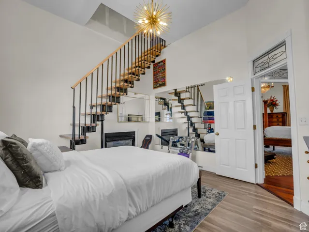 Bedroom with a chandelier, a glass covered fireplace, wood finished floors, and a high ceiling