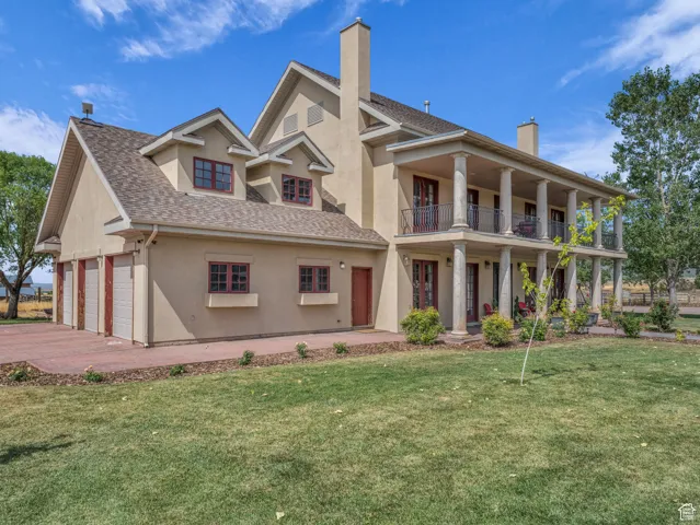 View of front facade featuring stucco siding, a balcony, a front lawn, driveway, and an attached garage
