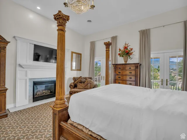 Bedroom with access to exterior, french doors, a chandelier, a fireplace with flush hearth, and recessed lighting