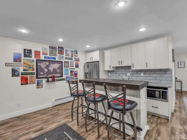 Kitchen with wood finished floors, appliances with stainless steel finishes, a kitchen bar, dark countertops, and backsplash