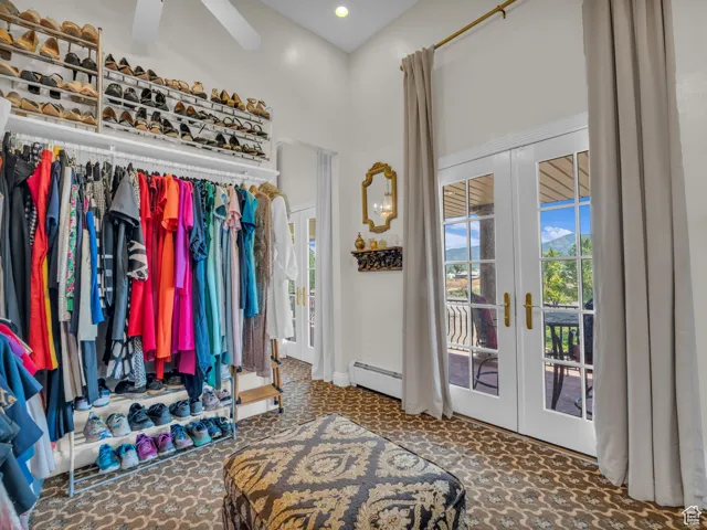 Walk in closet featuring french doors, carpet, a high ceiling, a baseboard radiator, and a ceiling fan