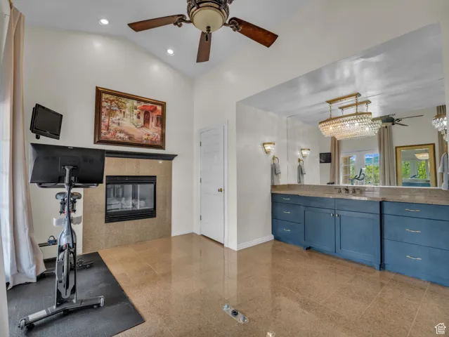 Bathroom featuring a ceiling fan, a tile fireplace, vanity, and lofted ceiling