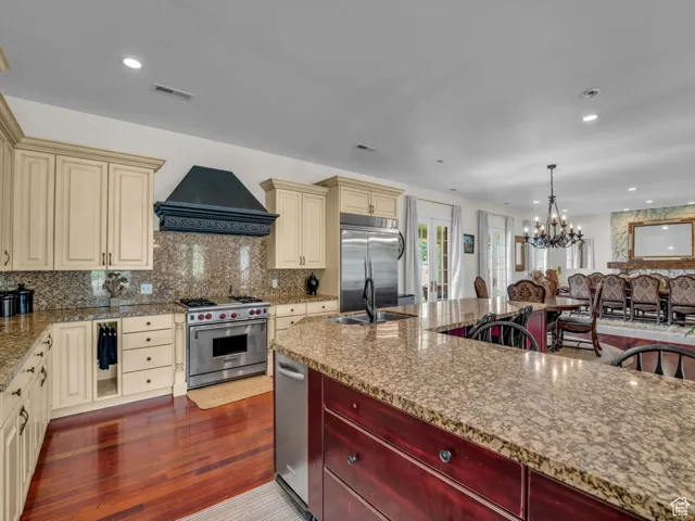 Kitchen with cream cabinets, a chandelier, high end appliances, decorative backsplash, and  hard wood flooring