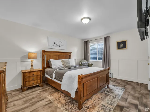 Bedroom with a decorative wall, a wainscoted wall, wood finished floors, and a baseboard heating unit