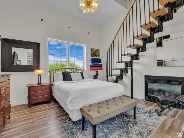 Bedroom with light wood finished floors, a high ceiling, and a glass covered fireplace