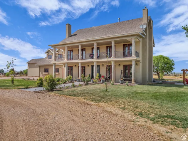 View of front of property featuring a chimney, a balcony, stucco siding, a front lawn, and roof with shingles
