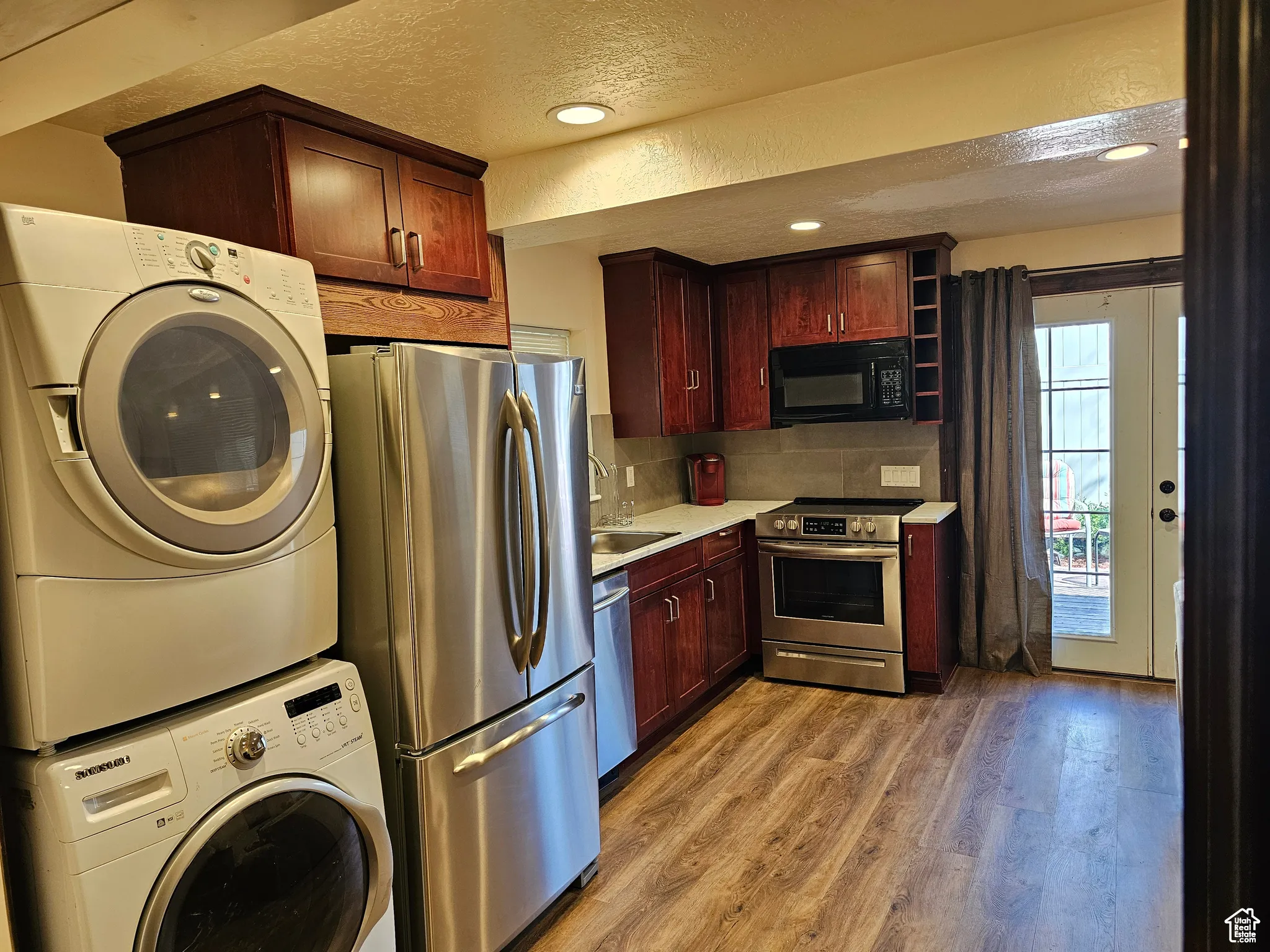 Kitchen with stainless steel appliances, stacked washing machine and dryer, light wood finished floors, a textured ceiling, and light countertops