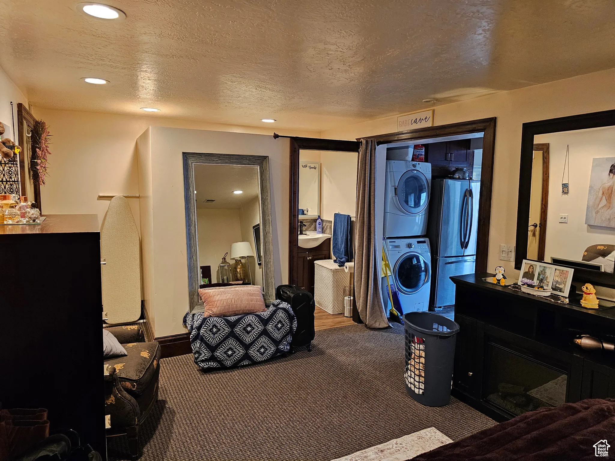 Carpeted bedroom featuring estacked washer and dryer, freestanding refrigerator, a textured ceiling, recessed lighting, and a fireplace