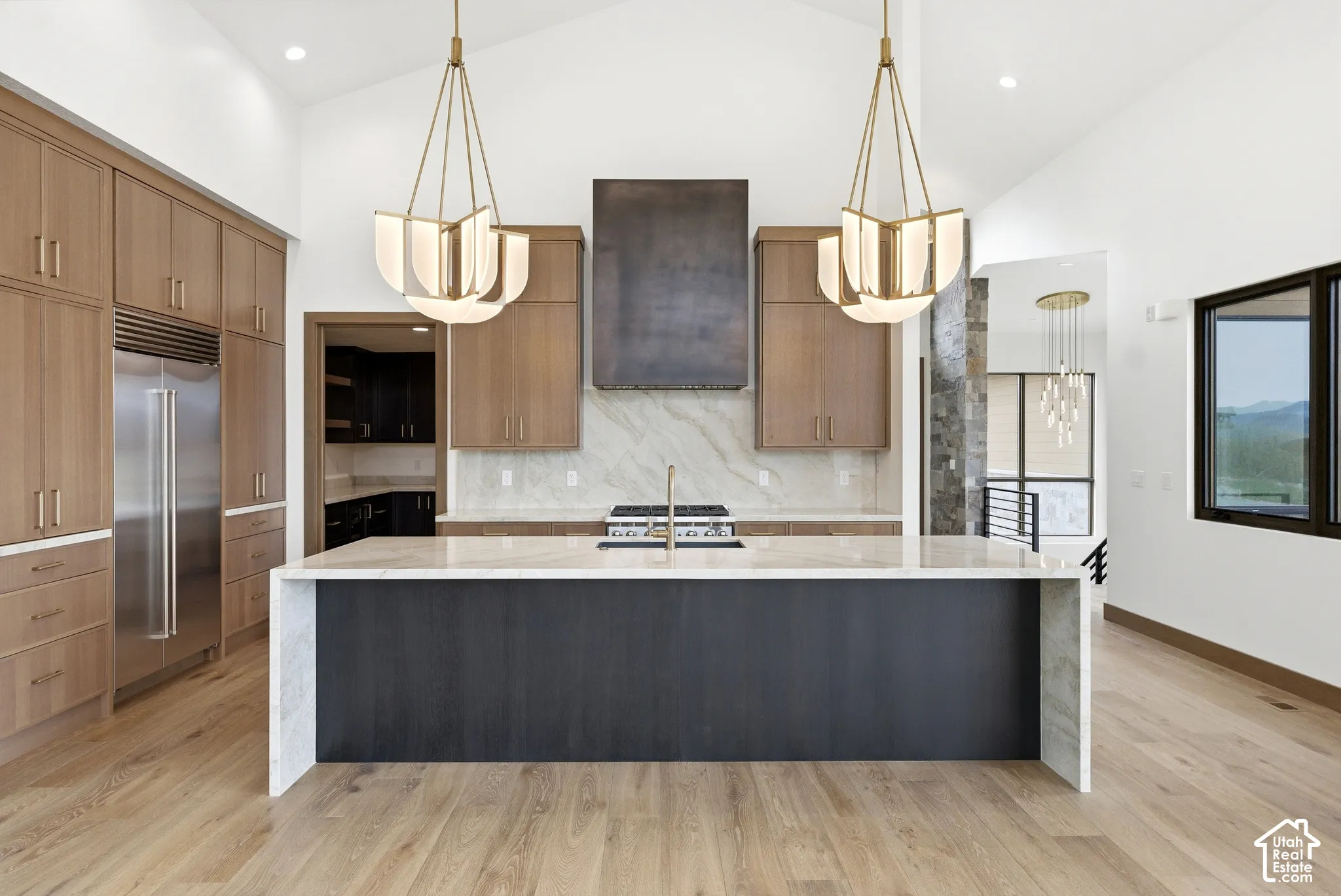 Open-concept kitchen featuring a large central island with a waterfall countertop, integrated stainless steel refrigerator, and wood-finish flooring