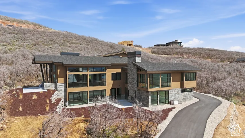Back of property with stone siding, a shingled roof, a chimney, and a sunroom
