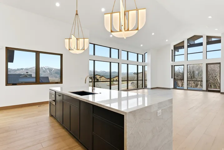 Kitchen featuring light wood-style floors, open floor plan, light stone counters, an island with sink, and a high ceiling